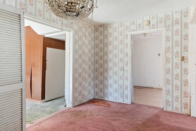 carpeted empty room featuring a textured ceiling and an inviting chandelier