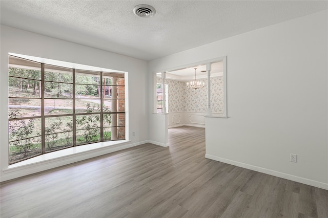 empty room featuring an inviting chandelier, hardwood / wood-style floors, and a textured ceiling