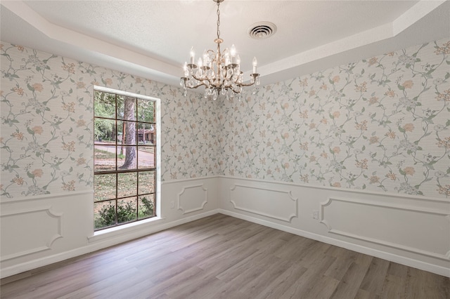 unfurnished room featuring a notable chandelier, wood-type flooring, and a tray ceiling