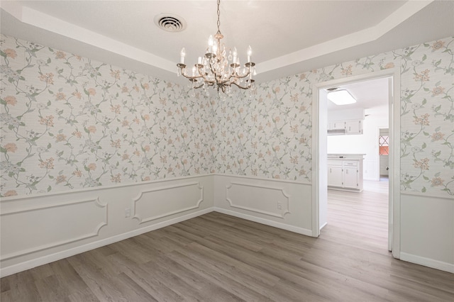 empty room with wood-type flooring, a tray ceiling, and a chandelier