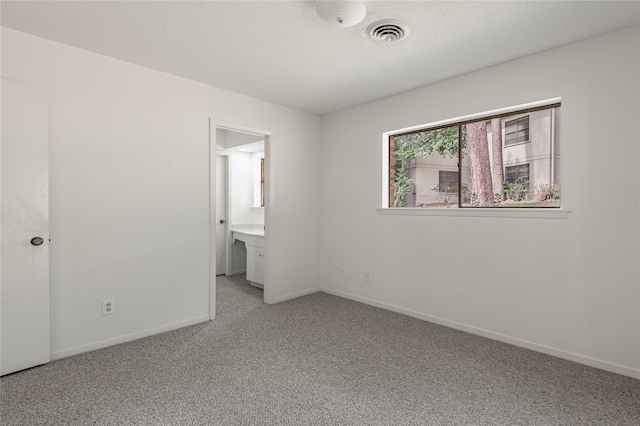 unfurnished bedroom featuring ensuite bath, carpet, and a textured ceiling