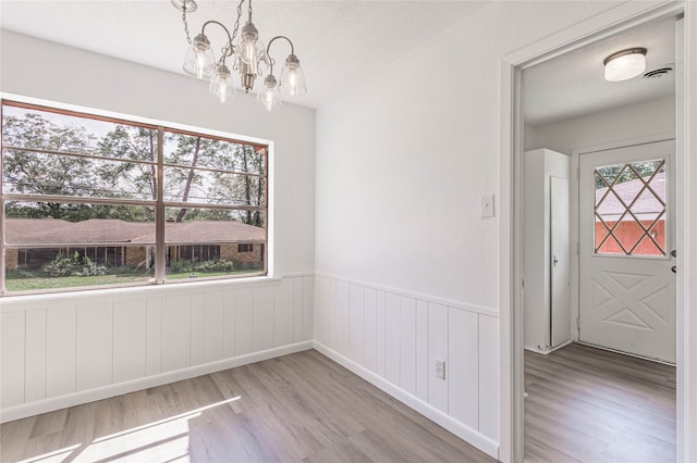 unfurnished dining area featuring light hardwood / wood-style flooring, a textured ceiling, and a chandelier