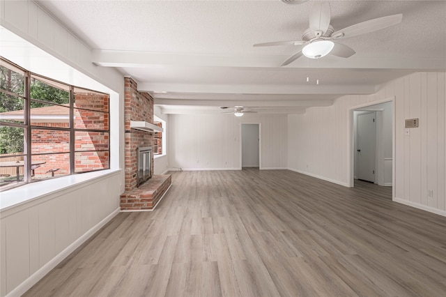 unfurnished living room featuring beam ceiling, a textured ceiling, a brick fireplace, and hardwood / wood-style flooring