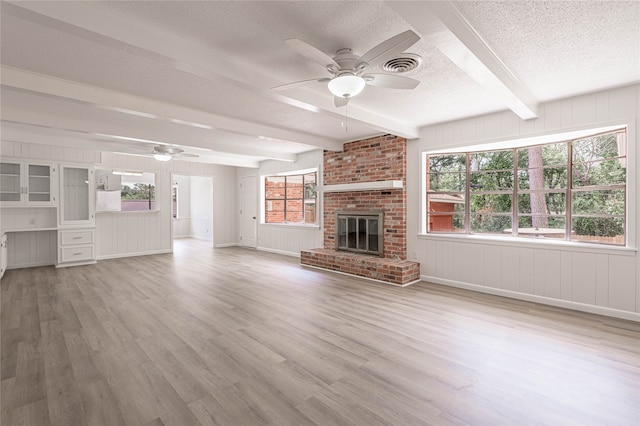 unfurnished living room featuring beam ceiling, wood-type flooring, a fireplace, and ceiling fan