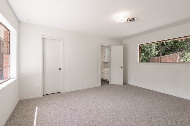 unfurnished bedroom featuring ensuite bathroom and light colored carpet