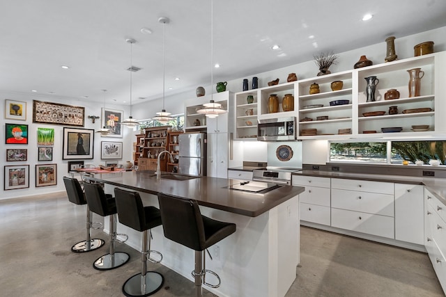 kitchen with a breakfast bar area, appliances with stainless steel finishes, an island with sink, white cabinetry, and sink