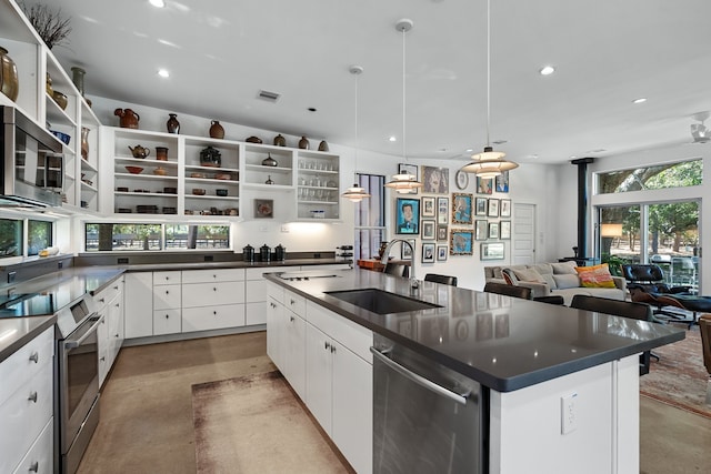 kitchen featuring a large island with sink, sink, white cabinetry, stainless steel appliances, and pendant lighting