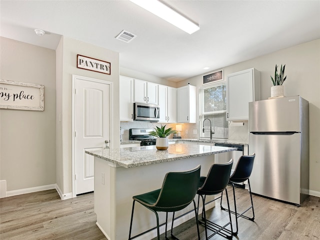 kitchen with a kitchen island, appliances with stainless steel finishes, white cabinetry, light stone countertops, and light hardwood / wood-style floors