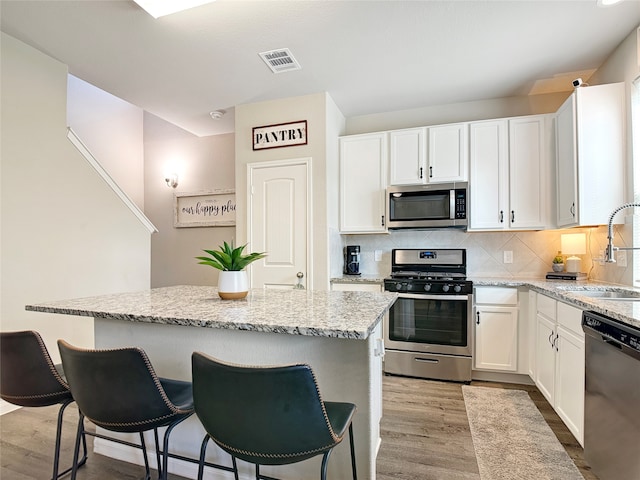 kitchen featuring appliances with stainless steel finishes, white cabinets, light wood-type flooring, and a kitchen island