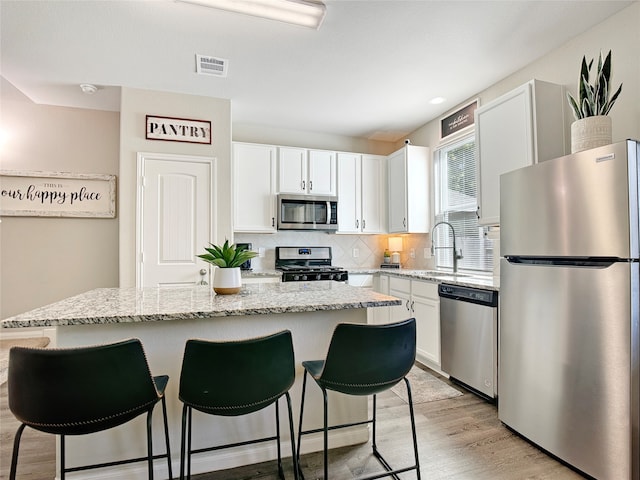 kitchen with white cabinetry, stainless steel appliances, light hardwood / wood-style flooring, and a kitchen island