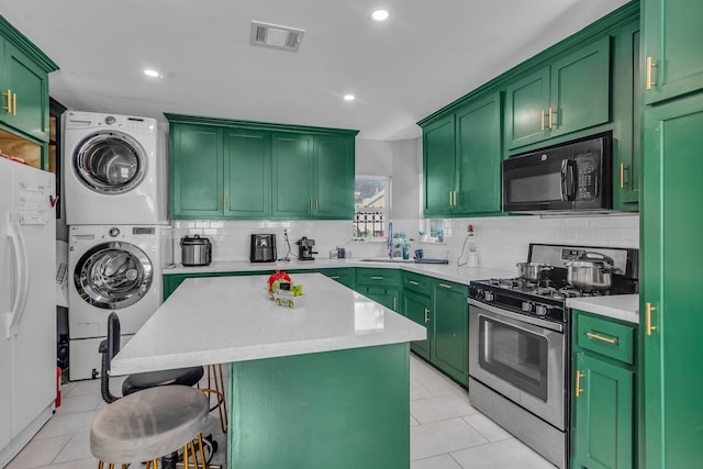 kitchen with white refrigerator, a center island, stacked washer / drying machine, green cabinetry, and stainless steel gas range