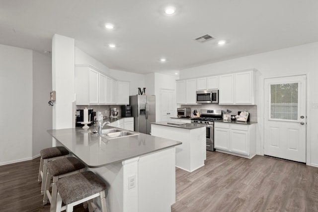 kitchen with a kitchen bar, stainless steel appliances, kitchen peninsula, sink, and light wood-type flooring