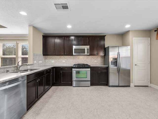 kitchen featuring sink, light stone countertops, appliances with stainless steel finishes, tasteful backsplash, and dark brown cabinets