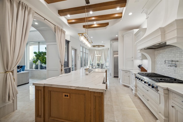 kitchen with stainless steel gas cooktop, decorative light fixtures, a kitchen island with sink, white cabinets, and premium range hood