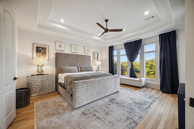 bedroom with a tray ceiling, ceiling fan, and light hardwood / wood-style flooring