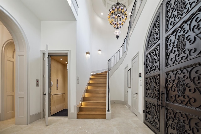 foyer entrance with an inviting chandelier, elevator, and a towering ceiling