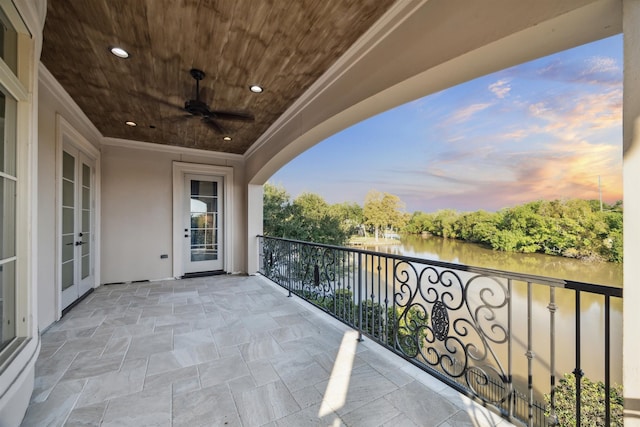 balcony at dusk featuring ceiling fan and a water view