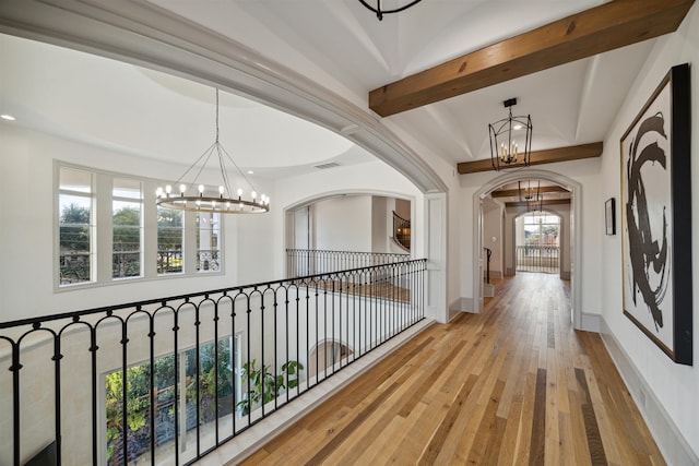 hall featuring a chandelier, beam ceiling, a wealth of natural light, and light hardwood / wood-style flooring