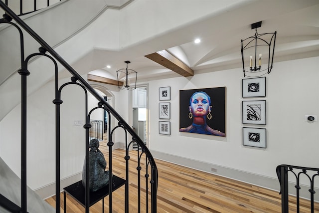 stairway with an inviting chandelier, hardwood / wood-style floors, and beam ceiling