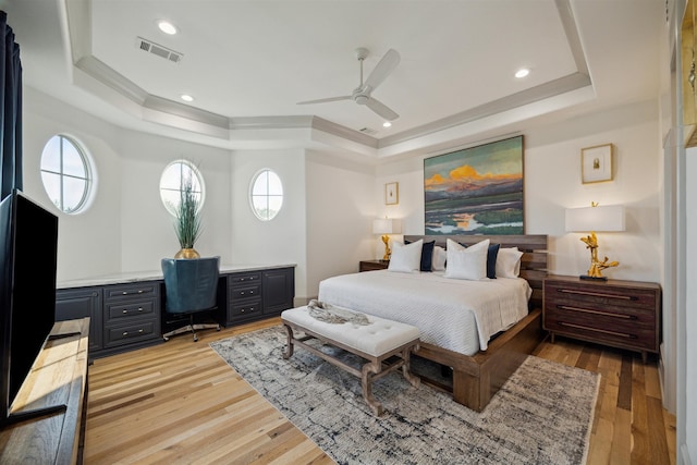 bedroom with light hardwood / wood-style floors, a tray ceiling, multiple windows, and ceiling fan