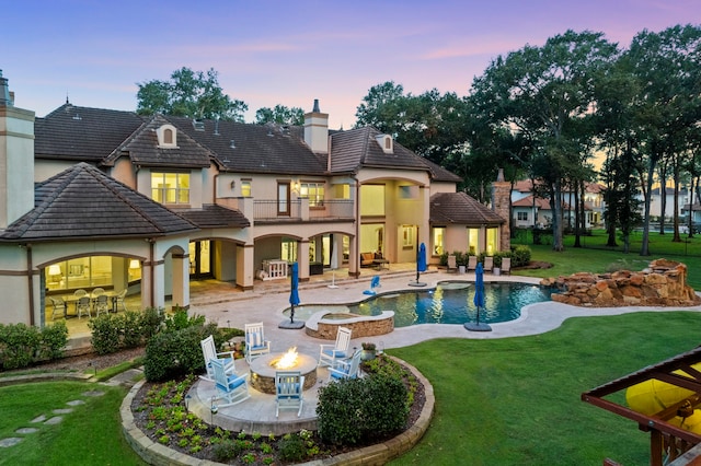 back house at dusk with a patio area, a fire pit, a lawn, and a balcony