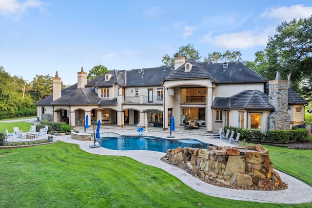 rear view of house with a balcony, a swimming pool with hot tub, a patio, and a lawn