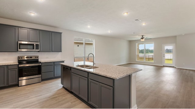 kitchen with an island with sink, stainless steel appliances, sink, and gray cabinetry