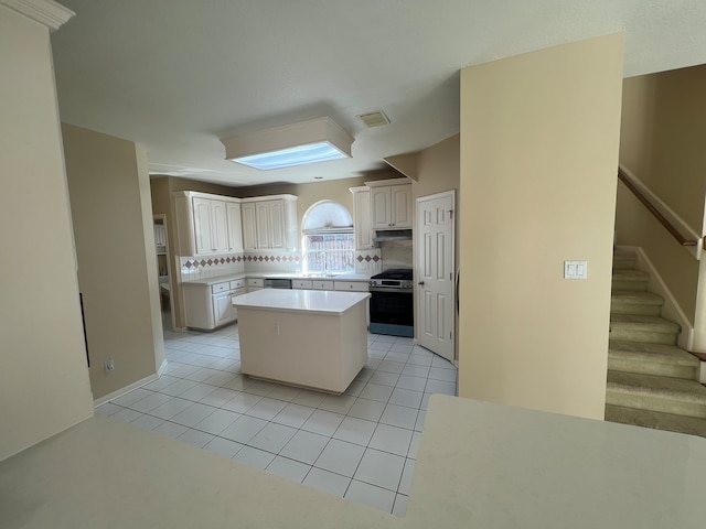 kitchen with light tile patterned floors, white cabinetry, backsplash, stainless steel range, and a kitchen island