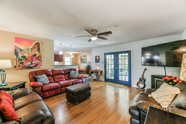 living room featuring french doors, a textured ceiling, light wood-type flooring, and ceiling fan