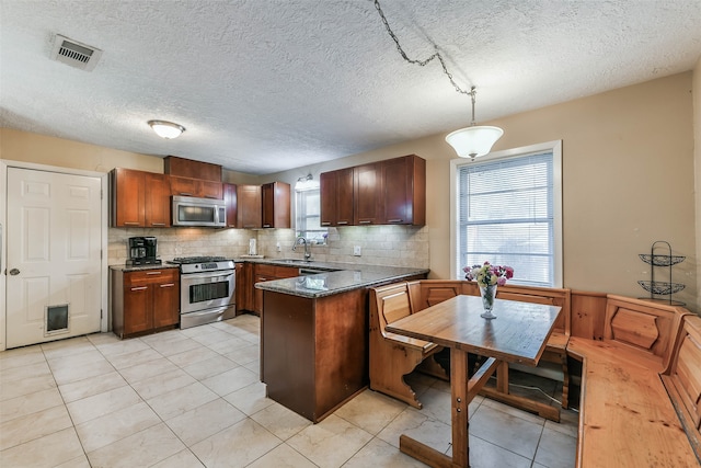 kitchen with appliances with stainless steel finishes, a textured ceiling, pendant lighting, decorative backsplash, and light tile patterned floors