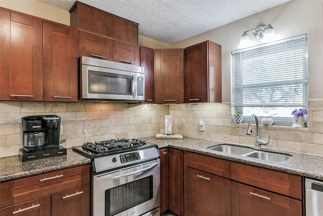 kitchen with backsplash, appliances with stainless steel finishes, a textured ceiling, dark stone countertops, and sink