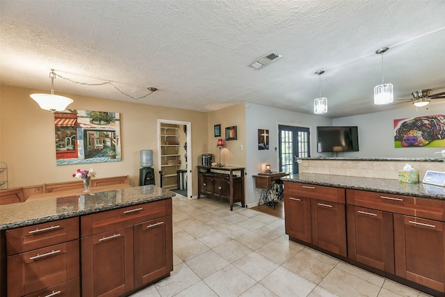 kitchen with light tile patterned flooring, hanging light fixtures, a textured ceiling, and dark stone countertops