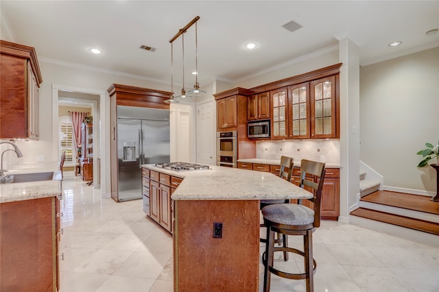 kitchen featuring stainless steel appliances, light stone counters, ornamental molding, a kitchen island, and pendant lighting