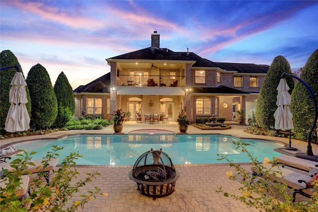 pool at dusk with a patio, a fire pit, and an in ground hot tub