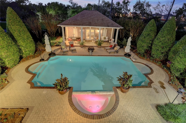 pool at dusk featuring an in ground hot tub and a patio area