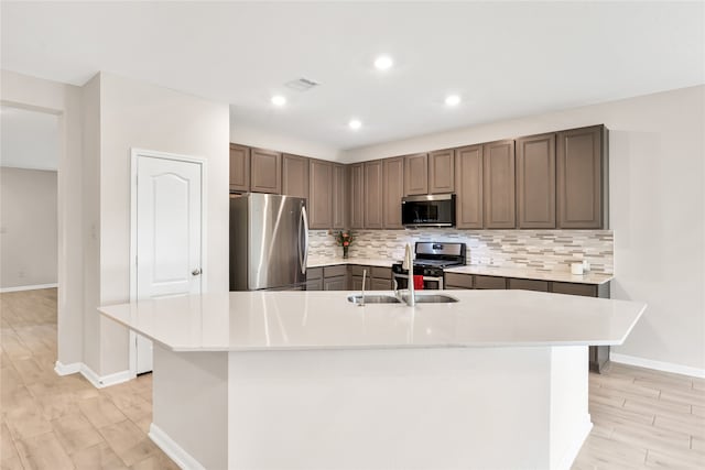 kitchen with appliances with stainless steel finishes, light hardwood / wood-style flooring, and a kitchen island with sink