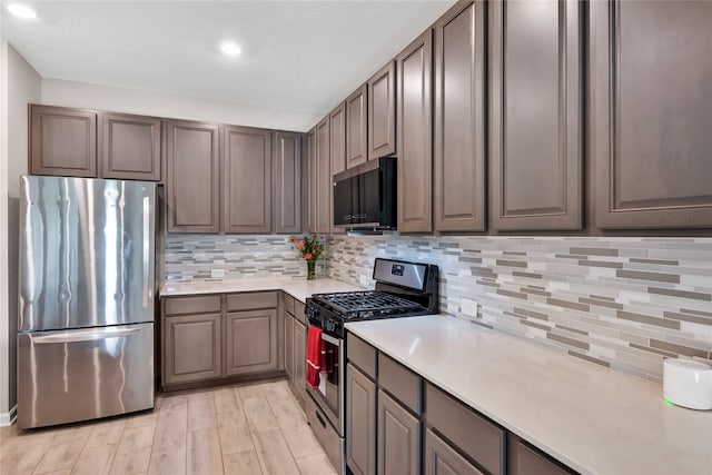 kitchen with appliances with stainless steel finishes, light wood-type flooring, and backsplash