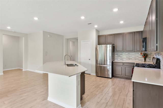 kitchen featuring sink, an island with sink, stainless steel appliances, and light wood-type flooring