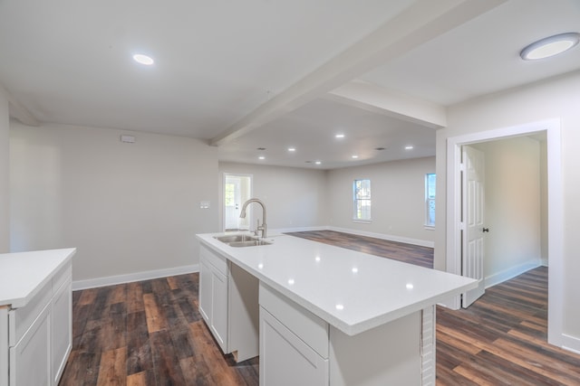 kitchen with dark wood-type flooring, sink, a center island with sink, beamed ceiling, and white cabinetry