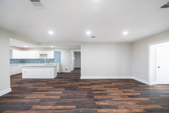 kitchen featuring white cabinets, decorative backsplash, dark hardwood / wood-style floors, and an island with sink