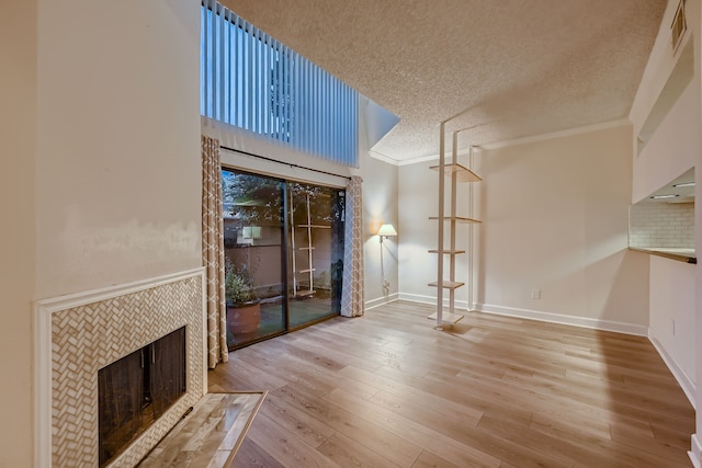 unfurnished living room with a tiled fireplace, a textured ceiling, ornamental molding, and hardwood / wood-style floors