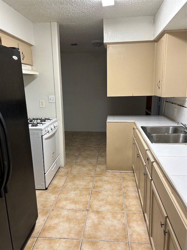 kitchen featuring sink, white gas range oven, a textured ceiling, black fridge, and light tile patterned floors