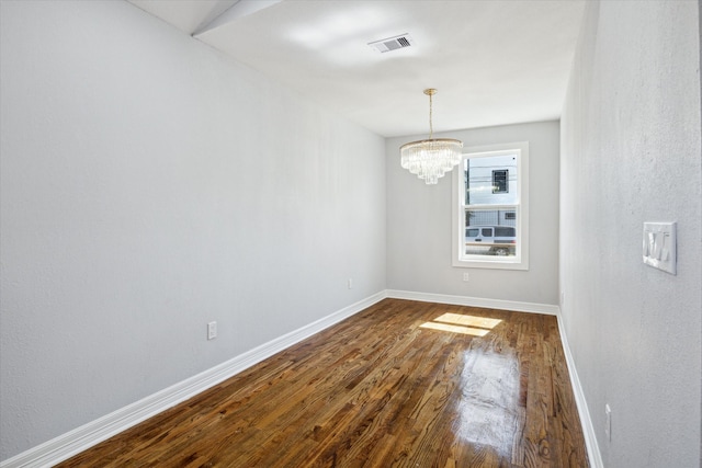 empty room with a notable chandelier and dark hardwood / wood-style flooring