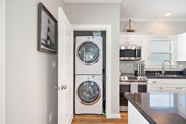 clothes washing area with light hardwood / wood-style floors, ornamental molding, stacked washer / drying machine, and sink