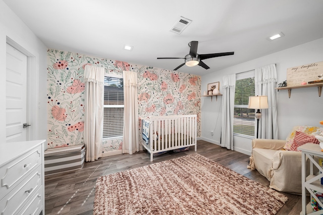 unfurnished bedroom featuring multiple windows, a nursery area, ceiling fan, and dark hardwood / wood-style floors