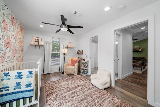 bedroom featuring dark wood-type flooring, a nursery area, and ceiling fan