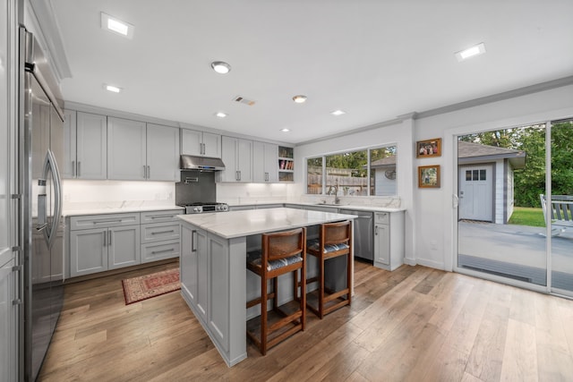 kitchen featuring a kitchen island, stainless steel appliances, ornamental molding, a breakfast bar, and light wood-type flooring