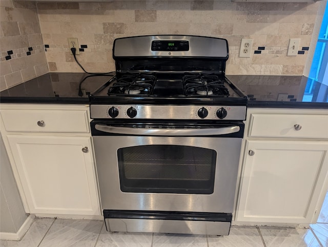 kitchen featuring gas stove, white cabinets, and backsplash