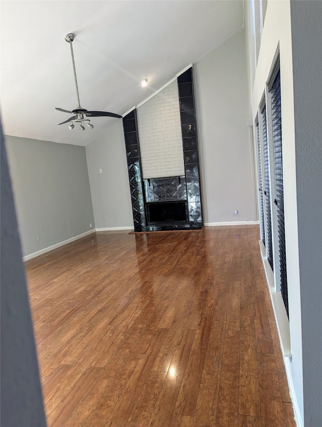 unfurnished living room featuring ceiling fan, hardwood / wood-style flooring, lofted ceiling, and a brick fireplace