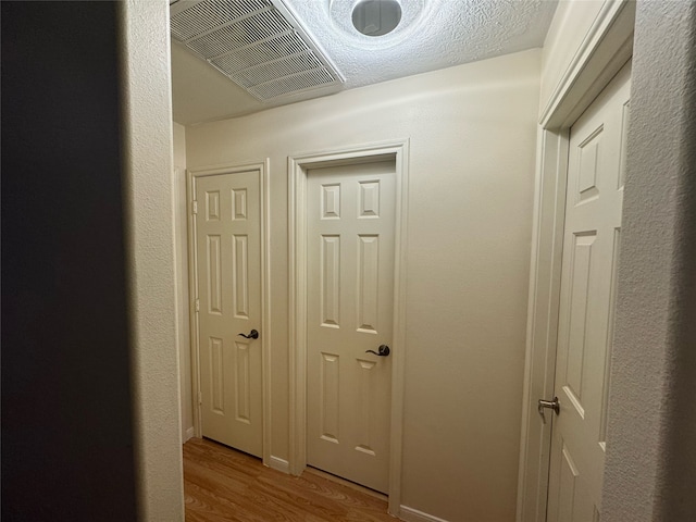 corridor with light hardwood / wood-style floors and a textured ceiling